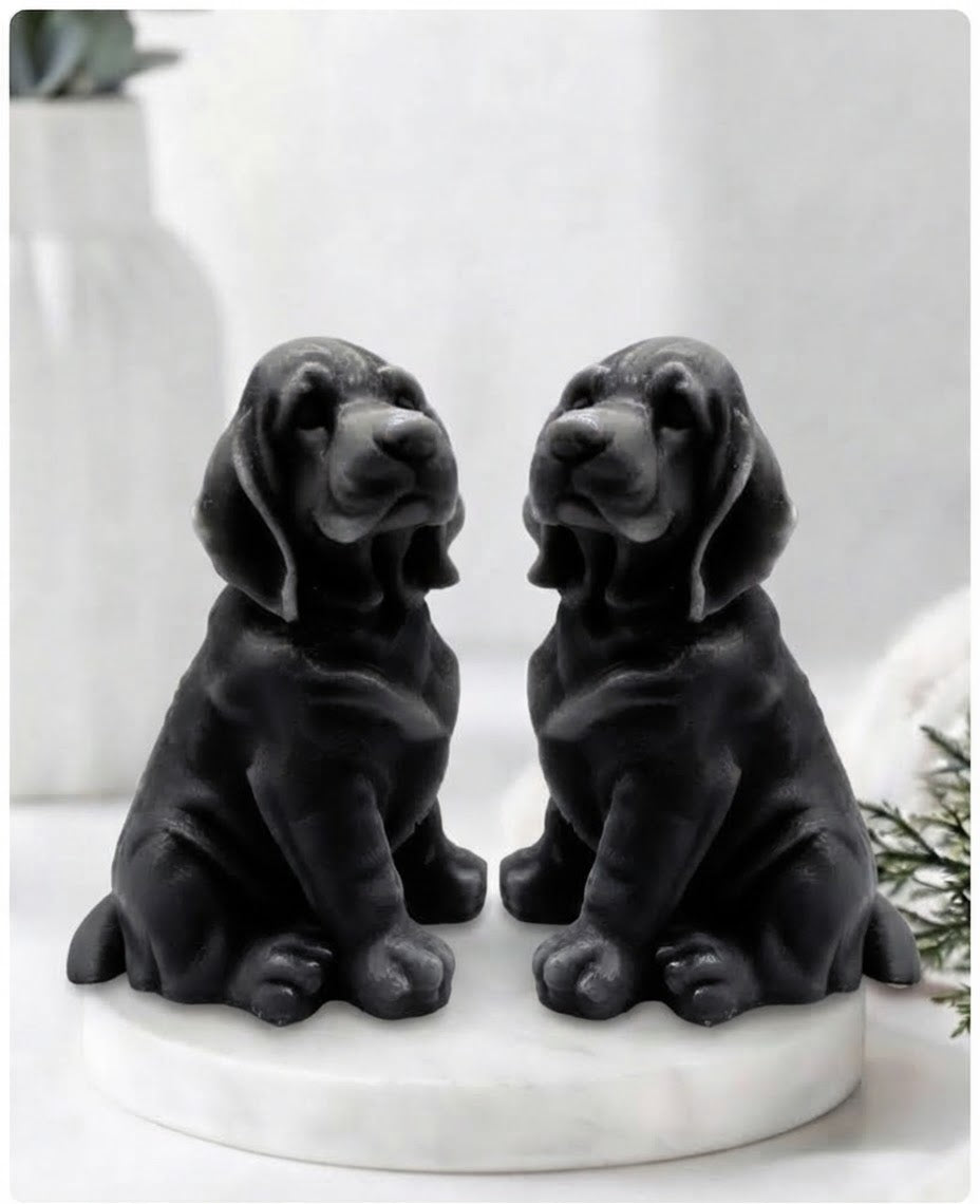 Two jet black bloodhound soaps sitting on a white marble display stand with a soft bathroom background.