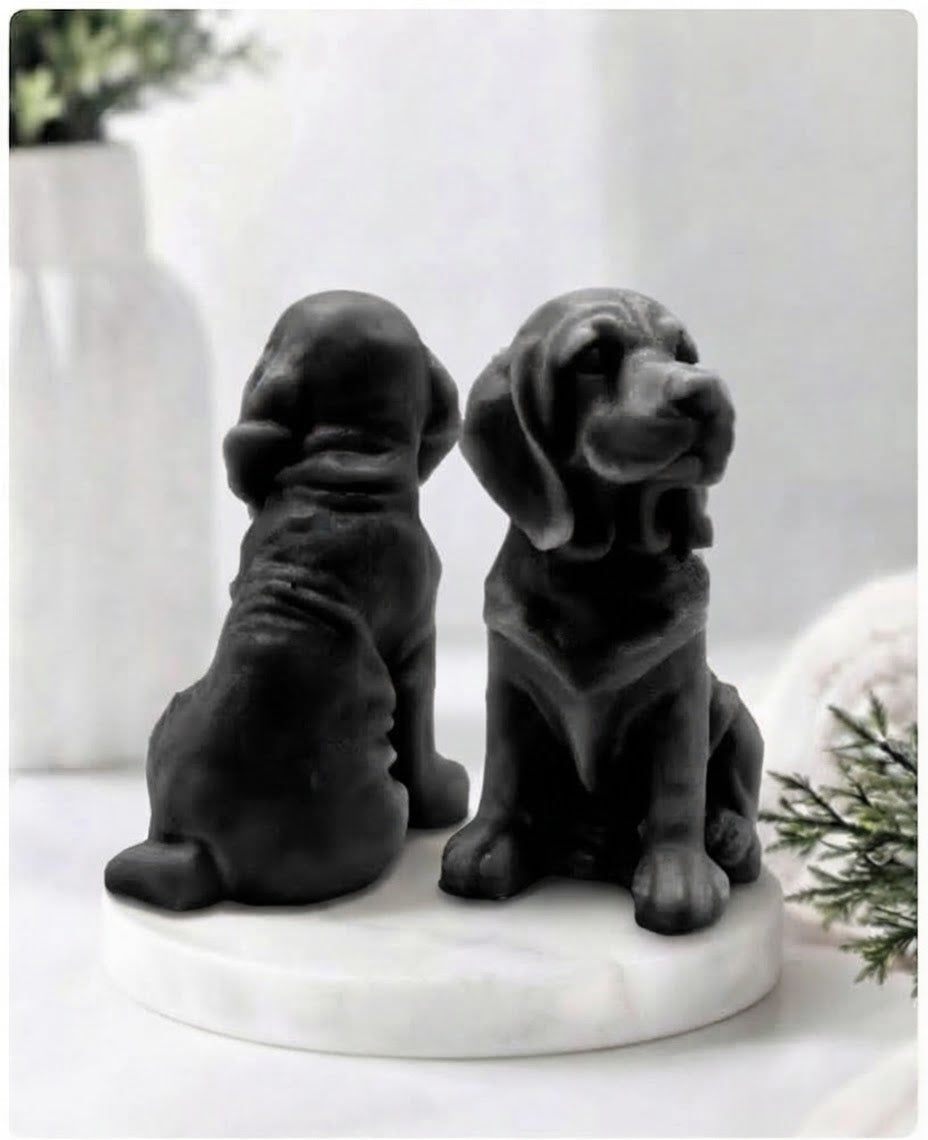 Two jet black charcoal bloodhound soaps sitting on a white marble display stand with a soft bathroom background