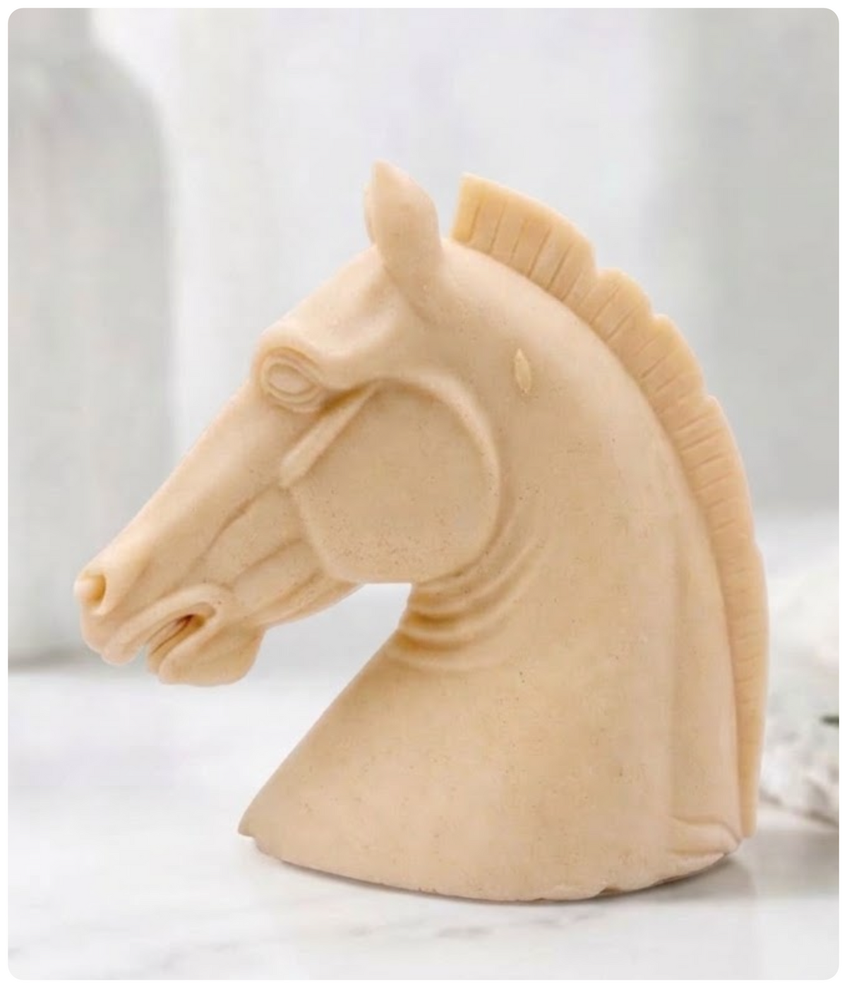 A yellow French clay horse head sculptural vegan soap, resembling a decorative chess piece or carved figurine, shown on a light marble-like surface with a soft blurred background.