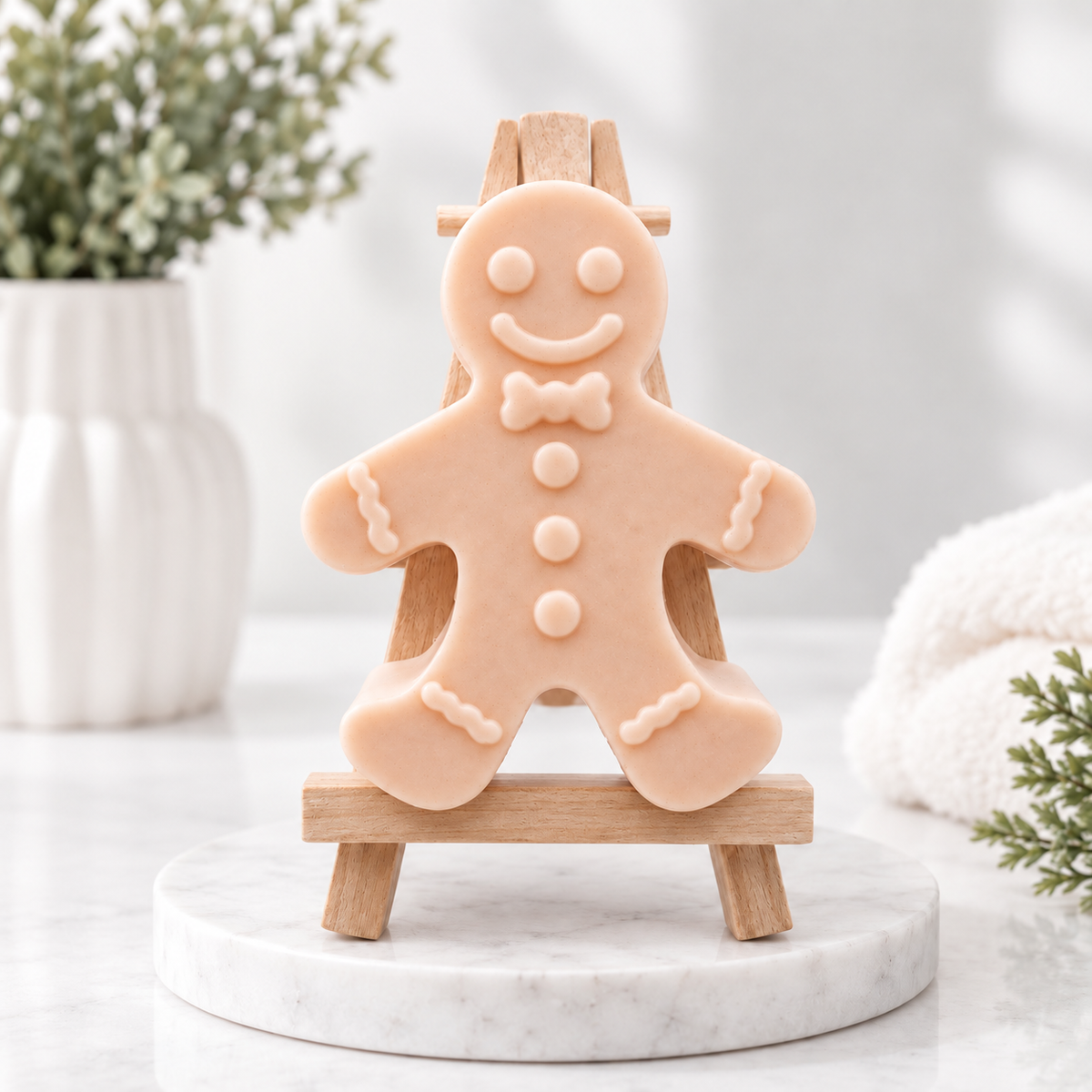A handmade vegan soap made with pink French clay, featuring a classic gingerbread man with a smiling face, a bow tie, and decorative icing details on his arms and legs, displayed on a miniature wooden easel.