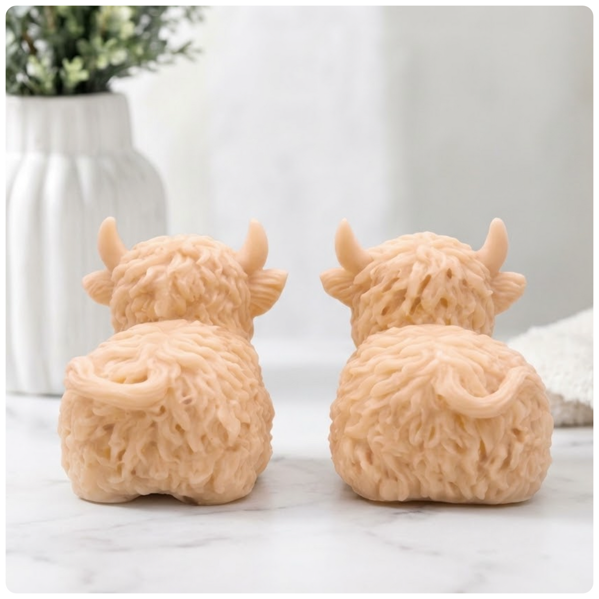 rear view of the two natural yellow French clay Highland cow vegan soaps, sitting side-by-side, with a very blurry background.