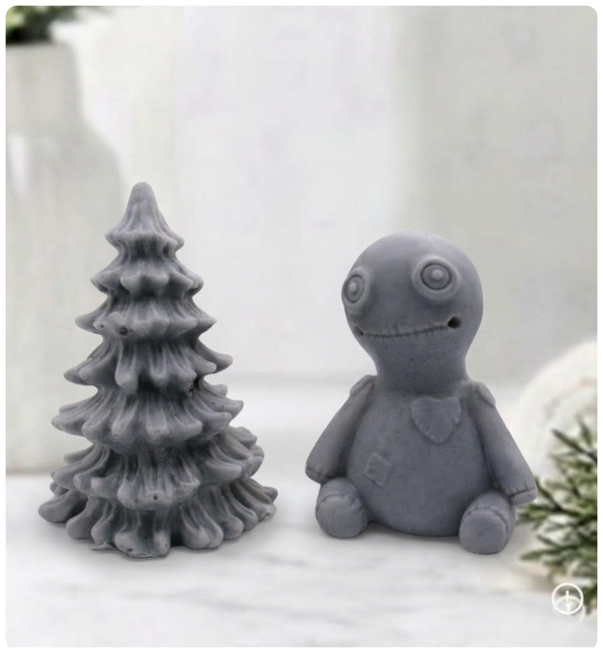 A handmade vegan soap gift set featuring a charcoal grey voodoo doll soap with stitched details and a activated charcoal grey tiered Christmas tree soap, presented in a black gift box tied with a red raffia ribbon and a small ladybird embellishment.