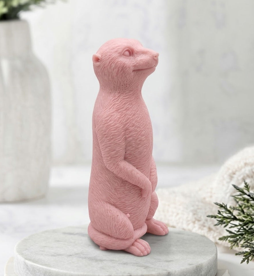 Handmade vegan meerkat soap figure made with pink French clay and standing on a marble display board.