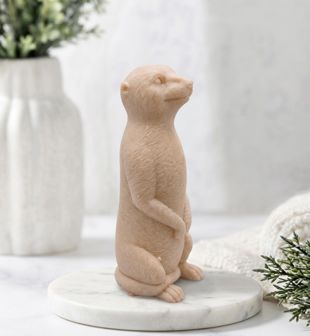 Handmade vegan meerkat-shaped soap standing upright made with yellow French clay, on a round marble display tray.