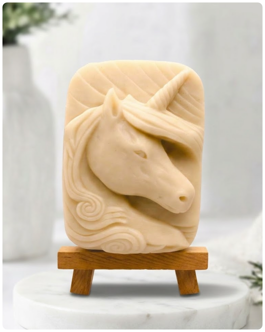 handmade vegan soap featuring a detailed unicorn head relief with a spiralled horn and flowing curly mane, made with yellow French clay and displayed on a small wooden easel. 