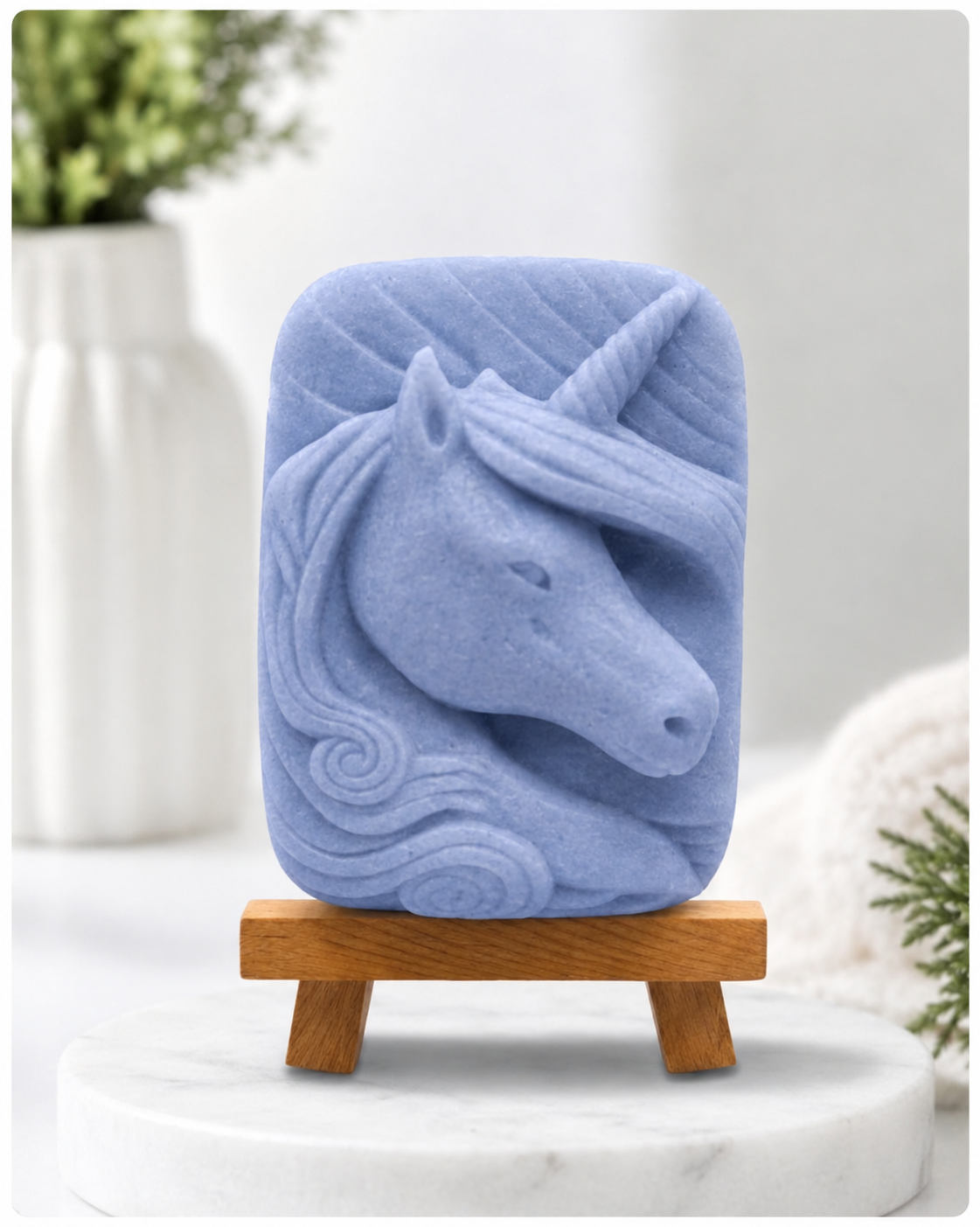 handmade vegan soap featuring a detailed unicorn head relief with a spiralled horn and flowing curly mane, made with indigo powder and displayed on a small wooden easel. 