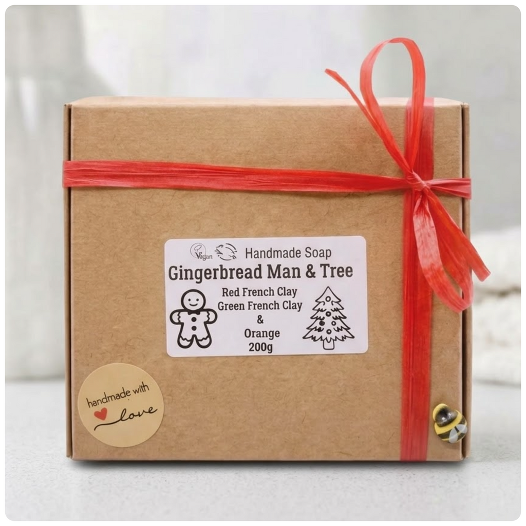Eco-friendly cardboard gift box containing the handmade vegan Gingerbread Man & Tree soap set, tied with a red raffia bow and decorative bee emblem