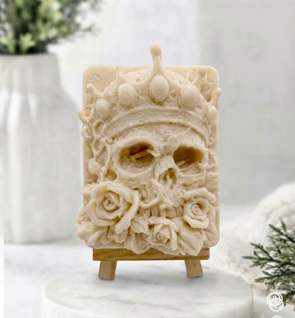 A detailed close-up of an intricate, yellow French clay vegan soap sculpture of a crowned human skull adorned with surrounding rose flowers, sitting on a small wooden display easel over a marble round plinth.