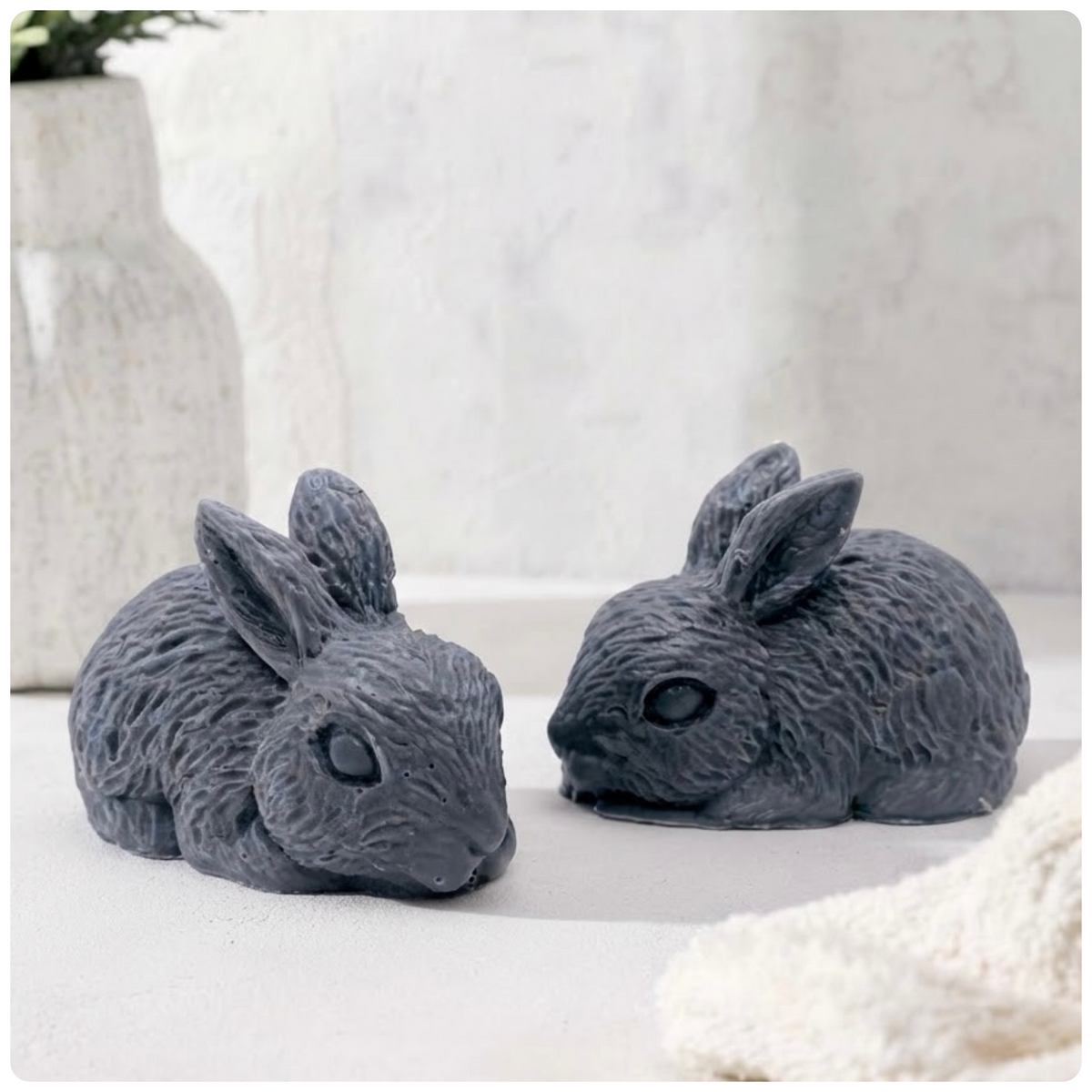 Two charcoal handmade rabbit soaps resting together on a pale marble platform.