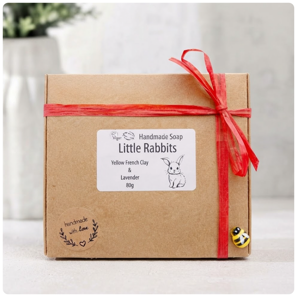 A brown paper gift box tied with a red ribbon, featuring a product label for handmade soap and a decorative bee charm.