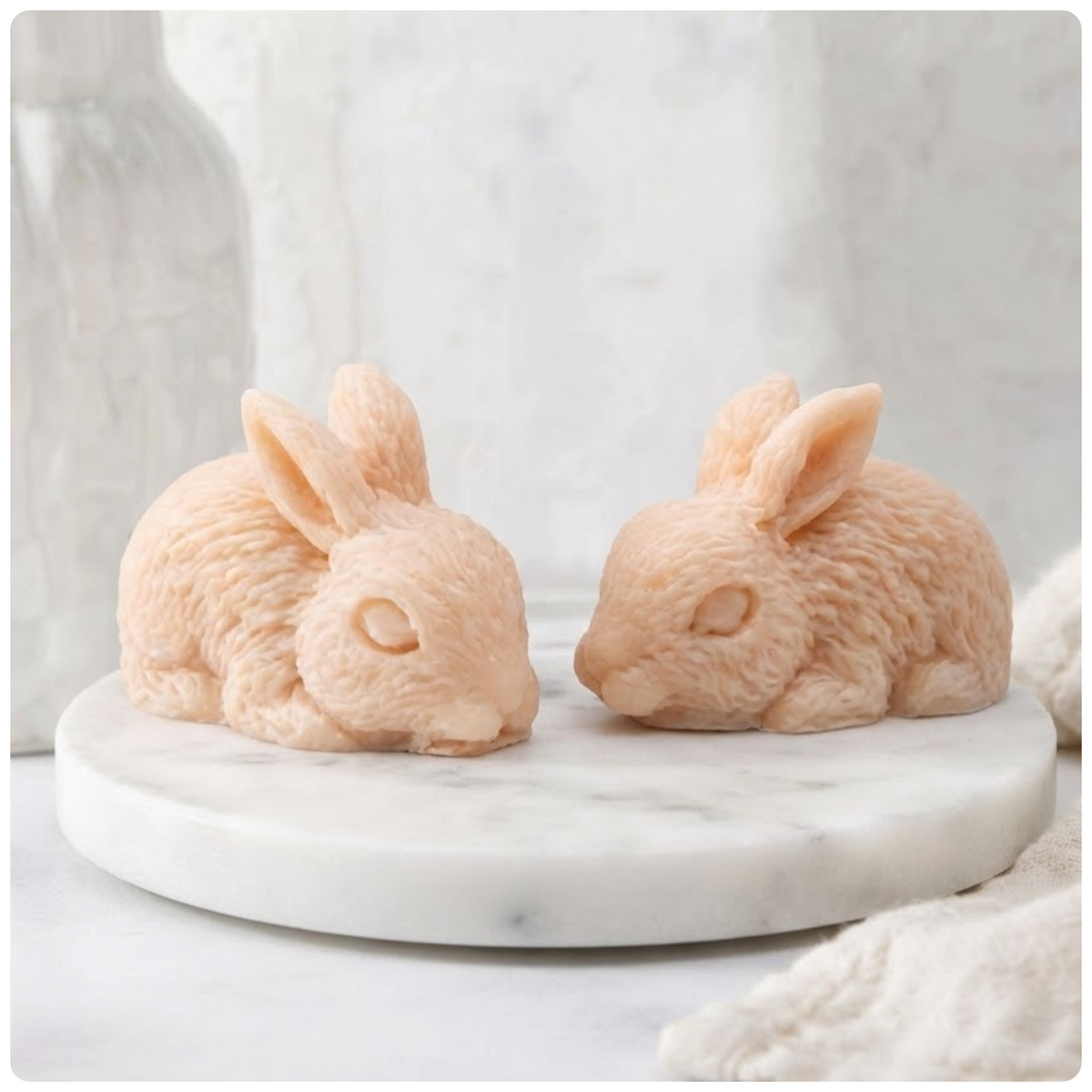 Two soft pink coloured handmade rabbit soaps positioned side by side on a round white marble tray.