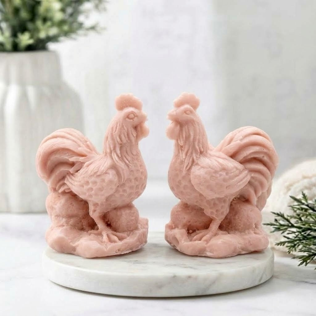 Two soft, pastel pink cockerel soaps, sculpted in detail from head to tail feathers, rest on the round white marble trivet. This image highlights the gentle, powdery pink color option and the delicate molded details of the bird figures.