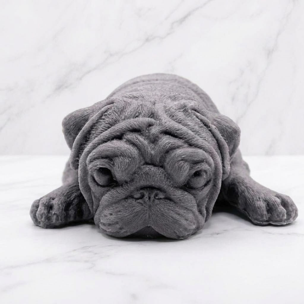 A front view of a charcoal grey pug-shaped vegan soap gift. resting on a light marble surface with a soft background.