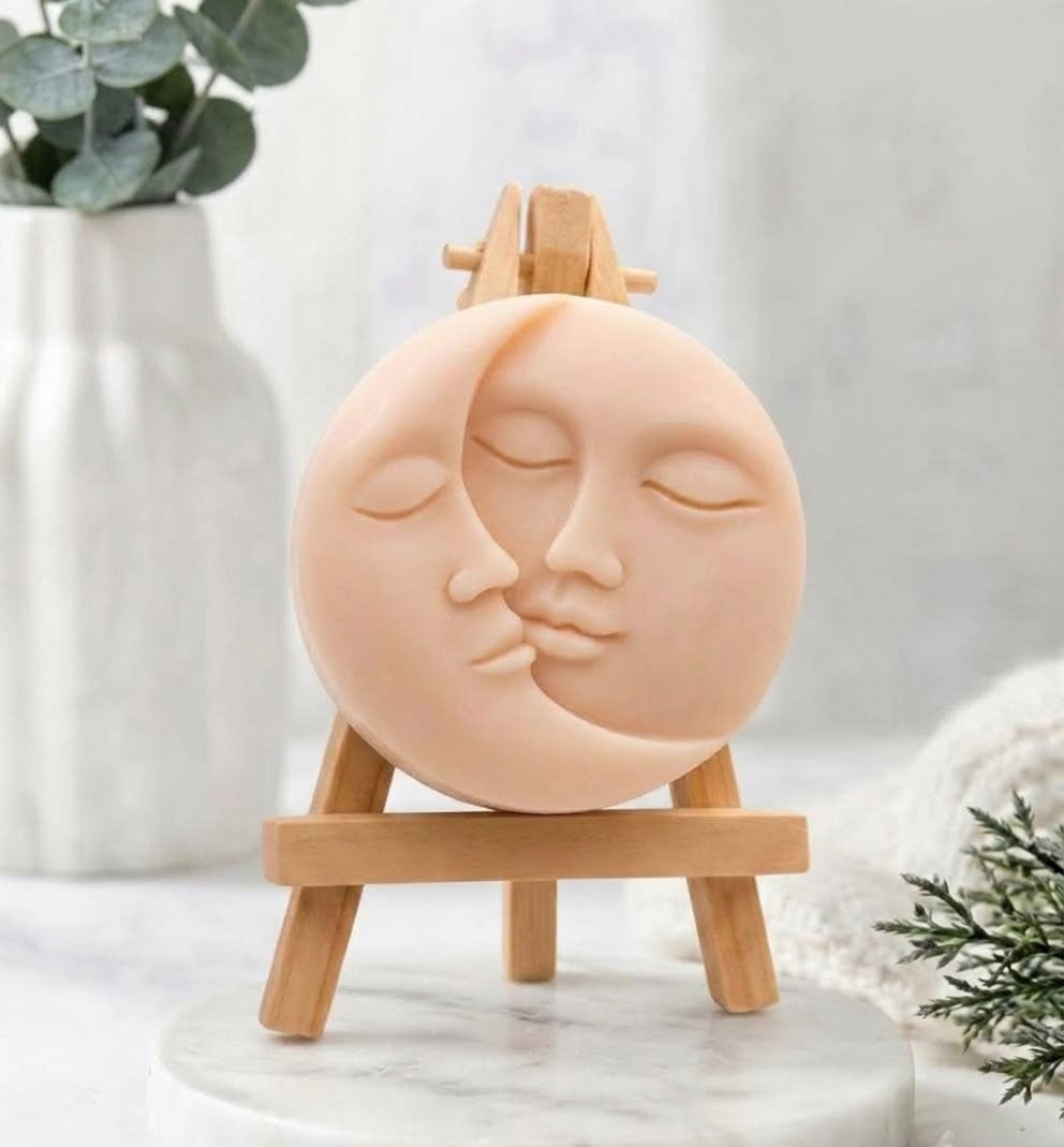 A soft pink-coloured, round vegan soap with a carved sun and moon kissing face.