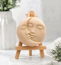 A cream-coloured, round vegan soap featuring a detailed sun and moon kissing face carving.