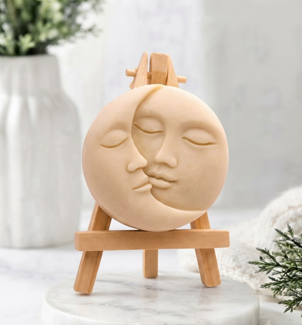A cream-coloured, round vegan soap featuring a detailed sun and moon kissing face carving.