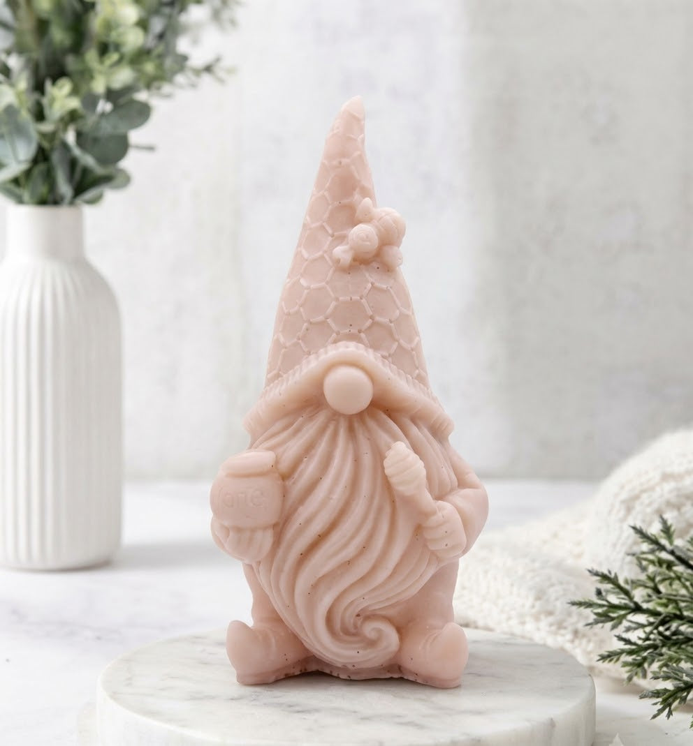 A close up shot of the pink-clay gnome-shaped vegan soap, shown sitting on a white marble pedestal, featuring its intricately carved honeycomb hat and tiny bee detail.