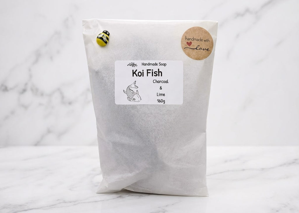 A white paper pouch of Koi Fish Charcoal & Lime activated carbon filter media, featuring a white label, a small bee sticker, and a round kraft paper seal, set against a white marble background.