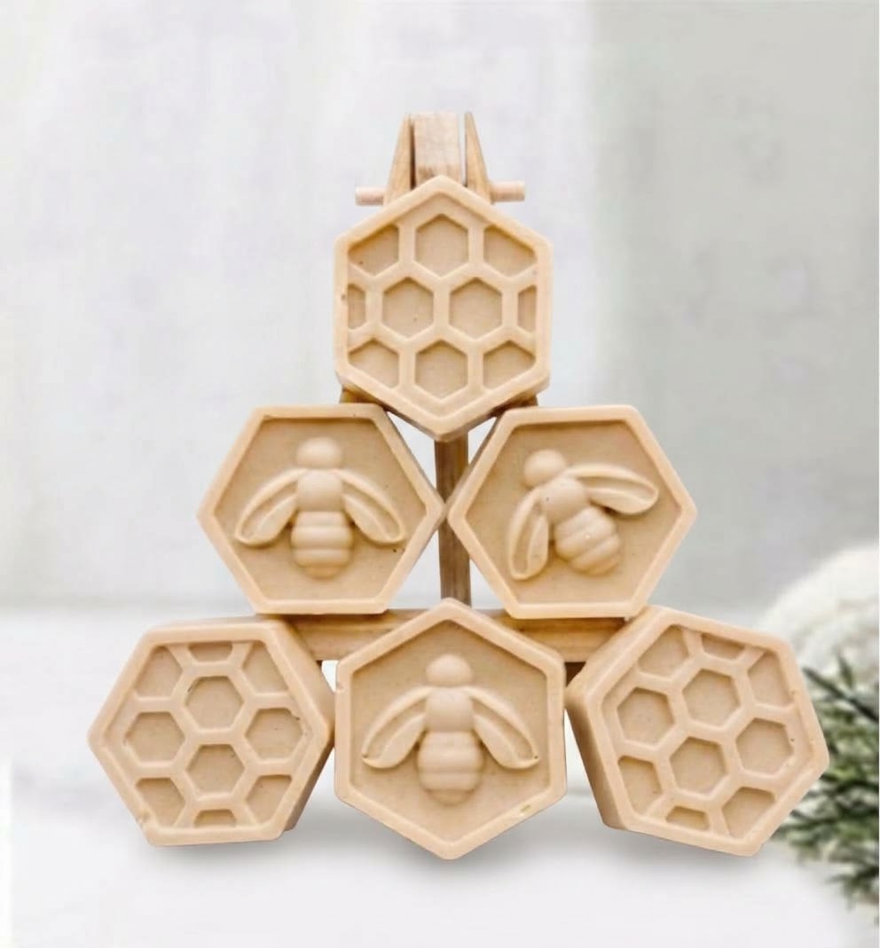 Six natural yellow soap bars shaped like honeycomb cells, with three bars featuring raised bee designs and three bars with honeycomb patterns, arranged in a pyramid on a light background.