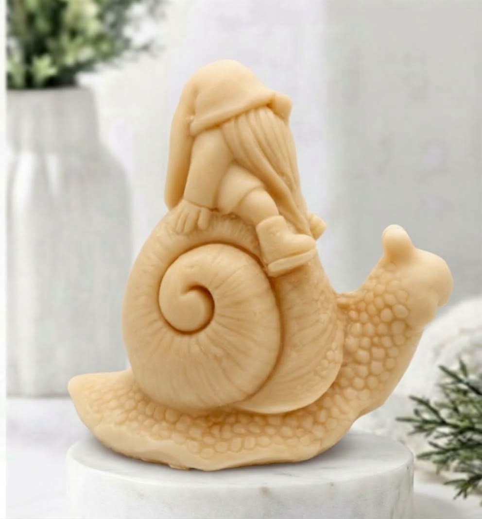 A soft yellow handmade vegan soap gift, sculpted as a whimsical gnome (gonk) with a tall, slouchy hat and a long beard, sitting on the shell of a large snail with a textured, bumpy body.