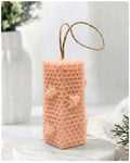 A pink-coloured honeycomb vegan soap with a natural jute hanging loop, displayed on a white marble pedestal against a soft, bright, blurred background.