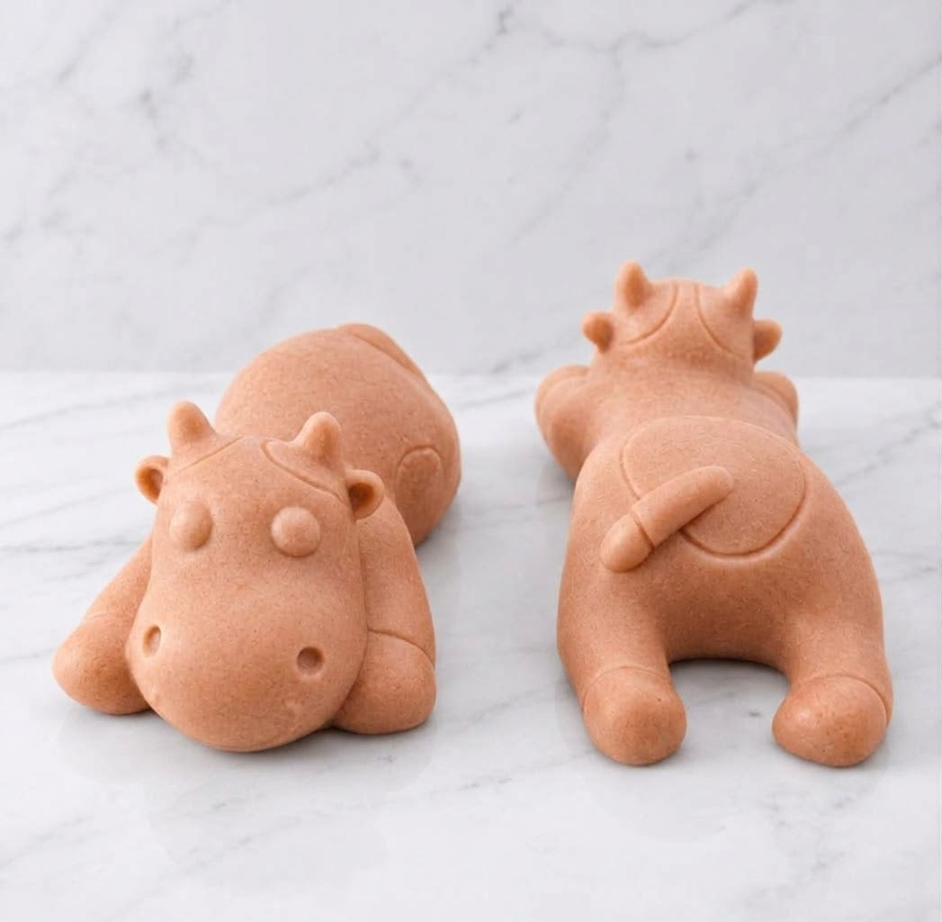 Two terracotta sleeping cow shaped soaps are resting side-by-side on a white marble countertop.