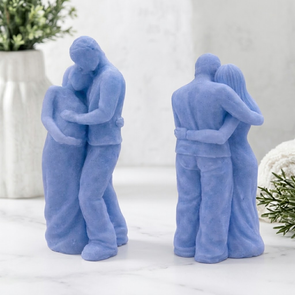 A front and rear view of a soap sculpture. It depicts a man in pants and a shirt embracing a pregnant woman in a long dress from behind, with his hands over her belly. They are on a round marble stand