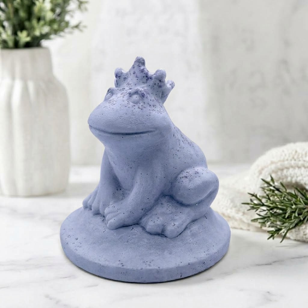 A side view of a soft blue handmade vegan soap featuring a frog prince with a crown on his head, displayed on a white background