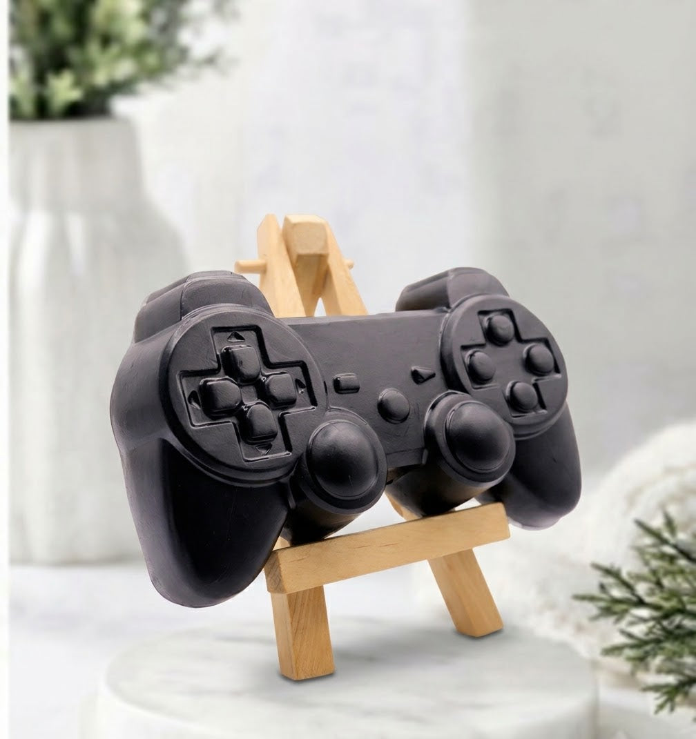 A jet black handmade vegan soap sculpted in the shape of a classic video game controller, finished in a deep charcoal black with realistic buttons and joysticks. 