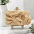 A rectangular soft yellow handmade vegan soap  featuring a high-relief carving of a Tyrannosaurus Rex with its jaws wide open in a roar and sharp claws framing the face, displayed on a miniature wooden easel.