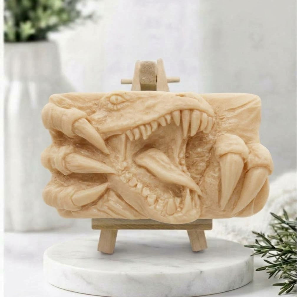 A rectangular soft yellow handmade vegan soap  featuring a high-relief carving of a Tyrannosaurus Rex with its jaws wide open in a roar and sharp claws framing the face, displayed on a miniature wooden easel.