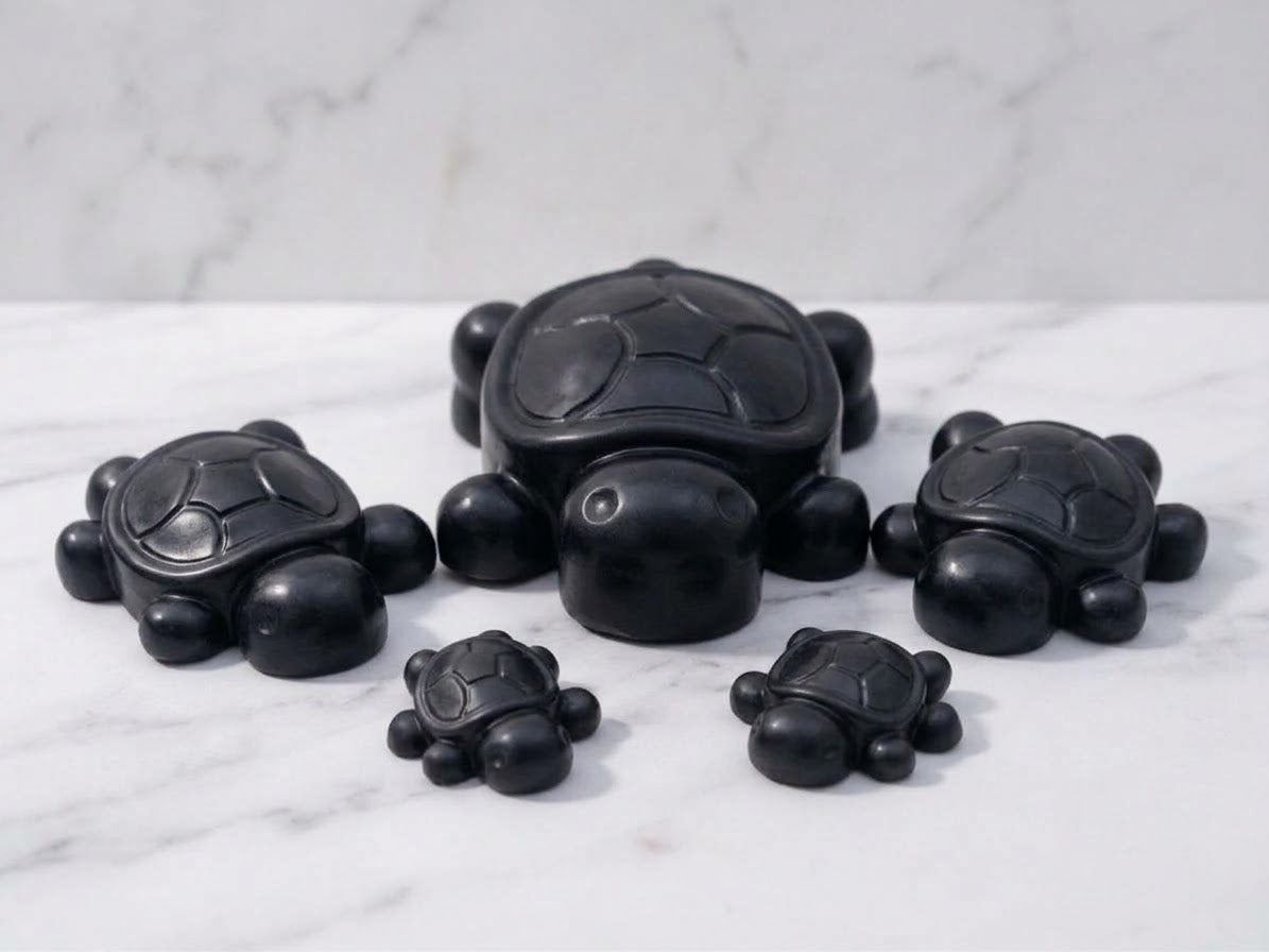A family-themed cluster of five Jet black coloured handmade turtle soap bars, including one large and two smaller pairs, resting on a white marble countertop. Unique animal soap gift set.