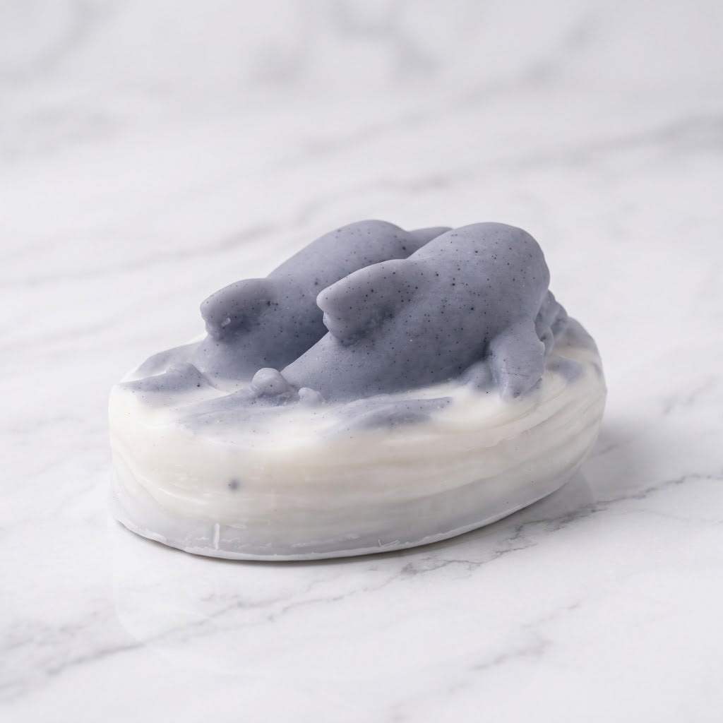 A three-quarter view of the ocean-themed vegan soap bar, showcasing the detailed texture of the two grey-blue speckled dolphins and the layered white waves, set against a marble backdrop.