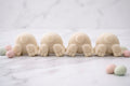 A line of four creamy yellow bunny tail vegan soaps on a white marble surface surrounded by scattered pastel mini speckled Easter egg decorations.