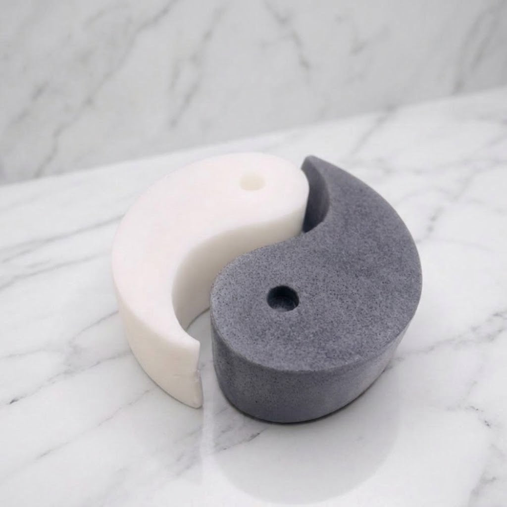 A handmade vegan soap gift set featuring two interlocking teardrop-shaped bars in contrasting black and white to form a large yin and yang symbol, displayed on a light wooden surface.