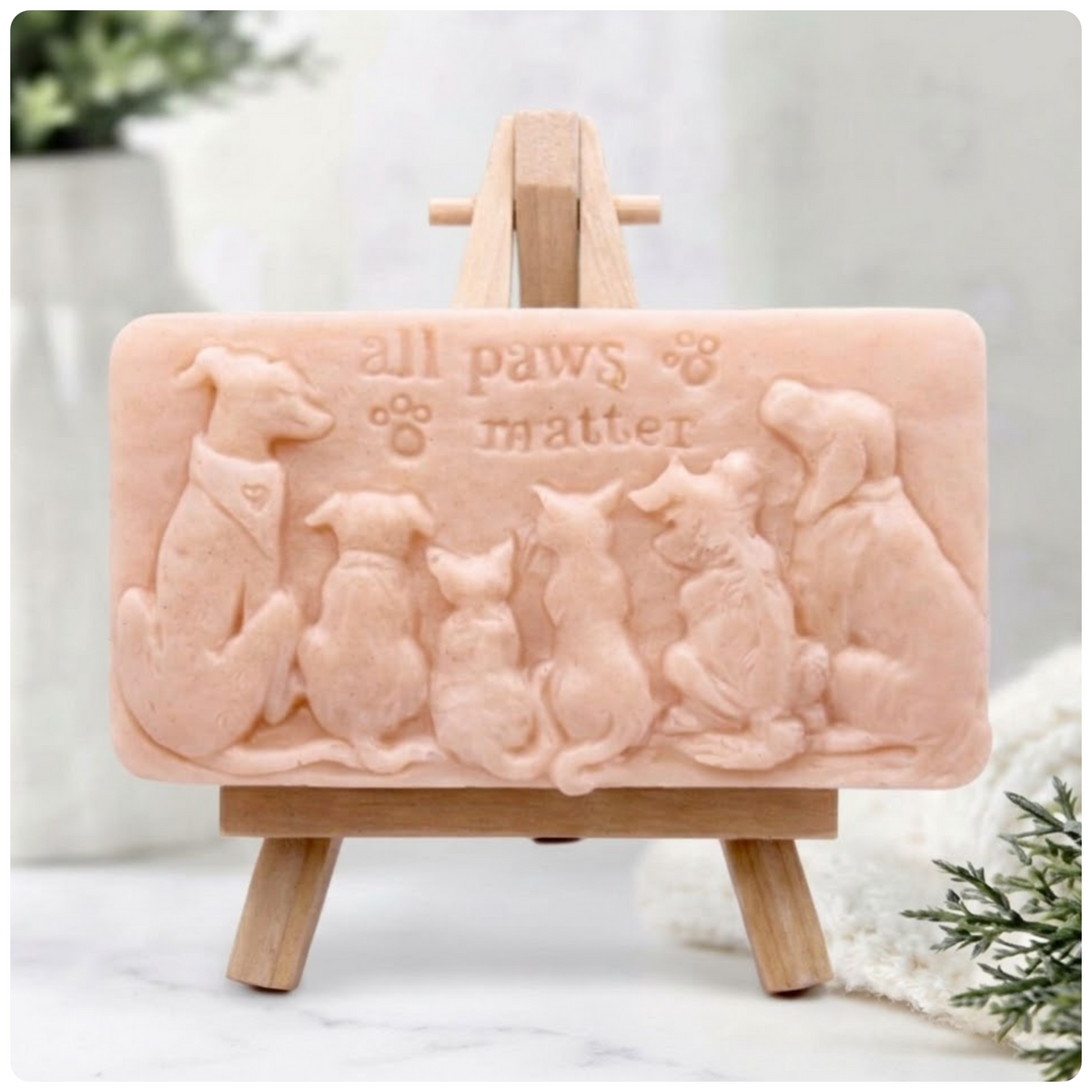 Handmade All Paws Matter vegan soap bar made with pink French clay and displayed on a wooden easel featuring an embossed pet design.