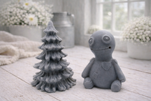 Load image into Gallery viewer, A handmade vegan soap gift set featuring a cream-coloured voodoo doll soap with stitched details and a grey tiered Christmas tree soap, presented in a black gift box tied with a red raffia ribbon and a small ladybird embellishment.
