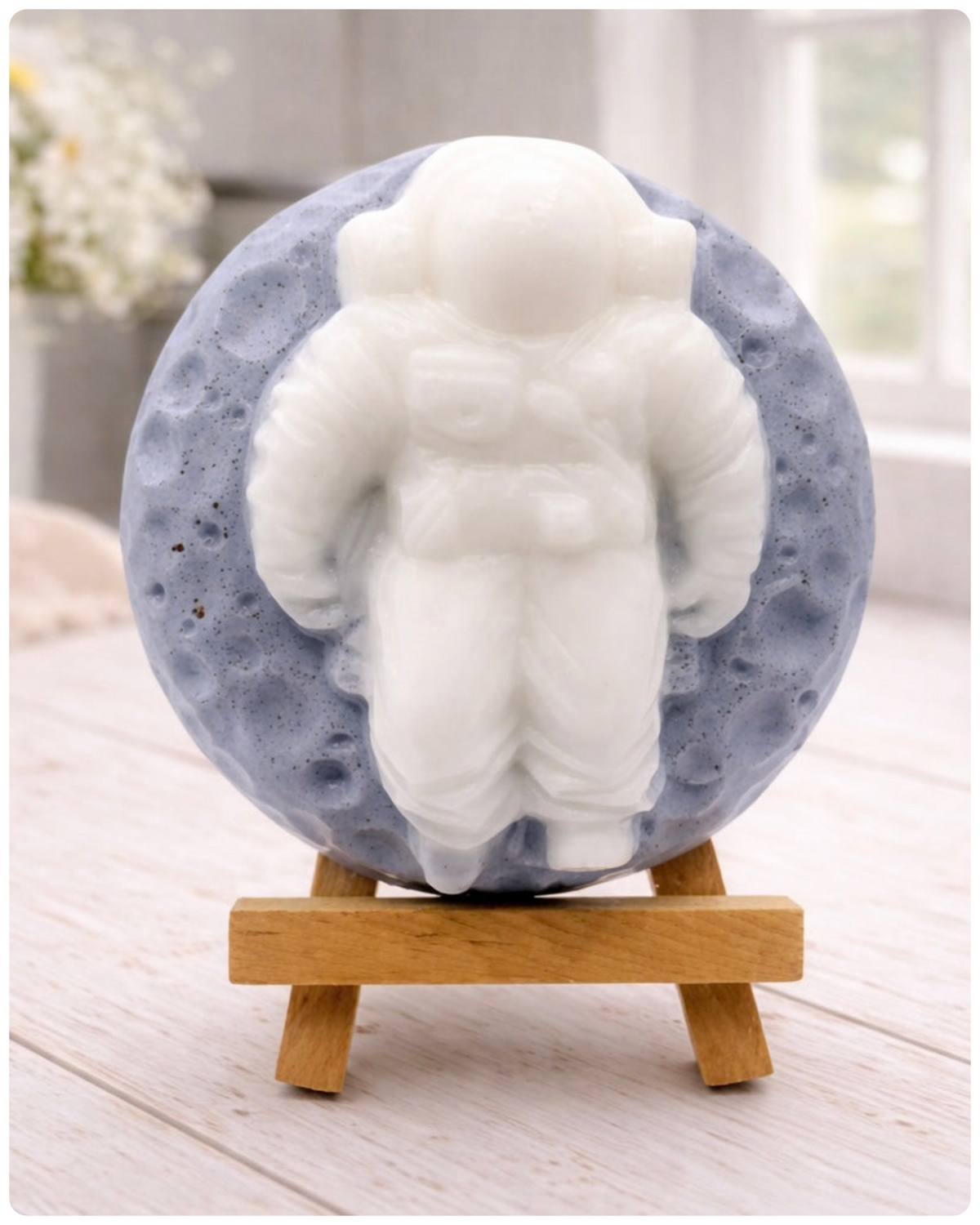 handmade vegan soap in the shape of a realistic astronaut sculpture sitting on the moon, featuring detailed spacesuit textures and craters on the lunar surface, displayed in a bright farmhouse decor setting.