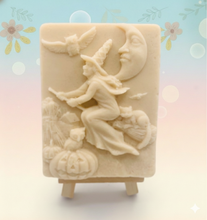 Load image into Gallery viewer, A beautiful handmade vegan soap featuring a detailed image of a witch flying on a broomstick past a crescent moon and owls, displayed on a wooden easel against a whimsical farmhouse decor background.
