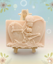 Load image into Gallery viewer, A spooky handmade vegan soap featuring a 3D relief of a skeleton relaxing against "RIP" tombstones, displayed on a wooden easel against a whimsical farmhouse decor background.
