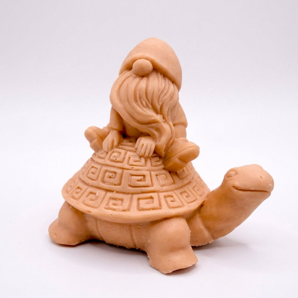A handmade vegan soap in a natural tone, sculpted as a whimsical gnome (gonk) with a long beard sitting on the back of a large, smiling turtle with a patterned geometric shell.