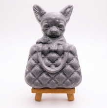 Load image into Gallery viewer, A highly detailed handmade vegan soap in a speckled grey marble finish, sculpted as a small chihuahua puppy with large ears peeking out from inside a quilted designer-style handbag, displayed on a miniature wooden easel.
