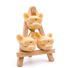 Load image into Gallery viewer, A set of three handmade vegan soaps in the shape of French Bulldog heads wearing sunglasses, displayed on a wooden easel in a bright, modern bathroom setting.
