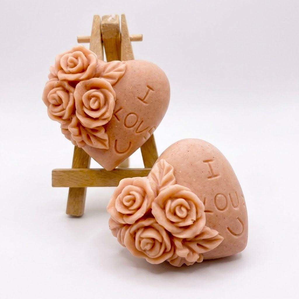 A handmade vegan soap gift set, featuring a central heart-shaped relief surrounded by a border of intricate rose flowers and delicate foliage, displayed on a small wooden easel.