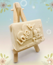 Load image into Gallery viewer, Handmade vegan soaps featuring a boy and girl sat on a bench with the wording Love Is... ,  in beautiful eco friendly packaging. crafted with natural French clays, activated charcoal and essential oils. a eco-friendly, zero waste gift that’s cruelty-free, skin-nourishing, the perfect gift for Valentines day or anniversary gift. small business UK
