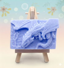 Load image into Gallery viewer, Dragon gift. Dinosaur gift. Our Flying Dragon soap features a striking dragon with its majestic wings spread wide, symbolising freedom and power. This artisan bar is vegan, cruelty-free, and designed with care for both your skin and the planet. Available in your choice of colour and essential oil. Each soap comes beautifully wrapped in eco friendly packaging. zero waste gift. kodern gift ideas. handmade home style. eco conscious home. eco friendly gifts. go green home. 
