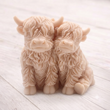 Load image into Gallery viewer, Handmade soap featuring two Highland cows with textured, shaggy fur sitting side by side on a light wooden surface with a softly indoor background.
