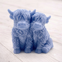 Load image into Gallery viewer, Handmade soap featuring two Highland cows with textured, shaggy fur sitting side by side on a light wooden surface with a softly indoor background.
