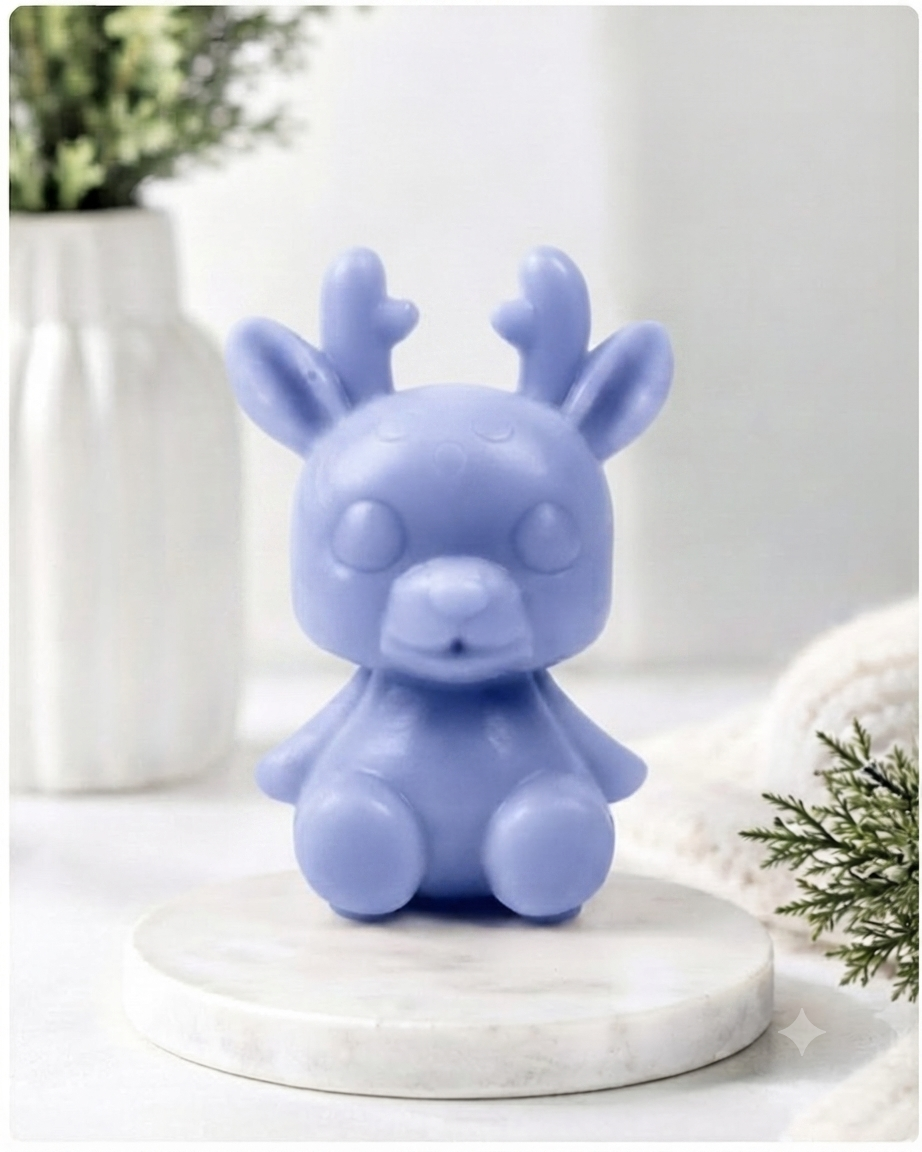 A 3D handmade vegan soap crafted into a cute, sitting baby reindeer with small antlers, rounded features, and a sweet expression, set against a bright farmhouse window.