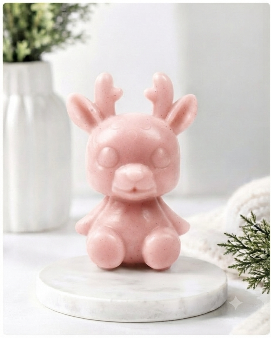 A 3D handmade vegan soap crafted into a cute, sitting baby reindeer with small antlers, rounded features, and a sweet expression, set against a bright farmhouse window.